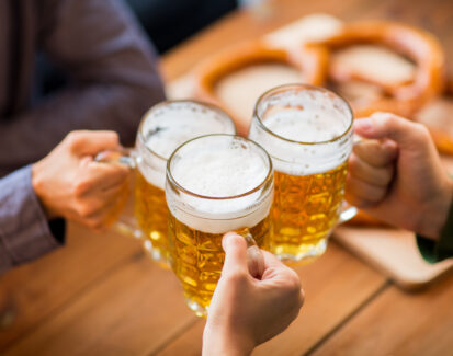 close up of hands clinking beer mugs at bar or pub